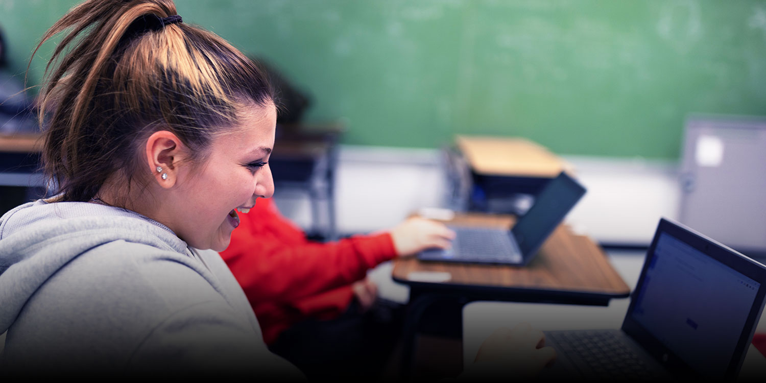 A high school student smiles as she looks at her laptop in class.
